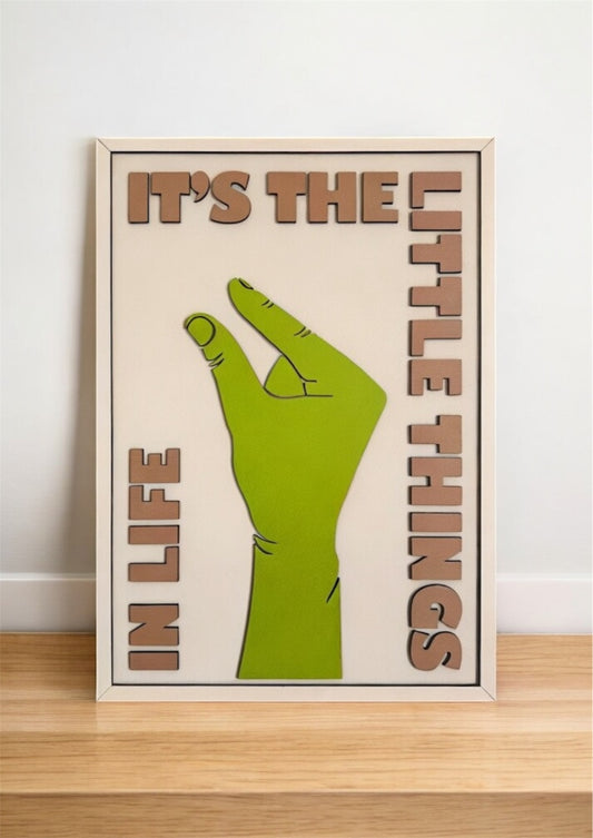 It’s the Little Things in Life wall art featuring a hand making the small sign, with a color palette of green, off-white, and sand. Perfect for minimalist home decor.