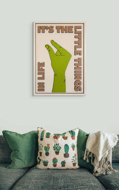 It’s the Little Things in Life wall art featuring a hand making the small sign, with a color palette of green, off-white, and sand. Perfect for minimalist home decor.